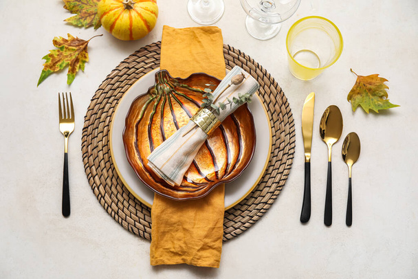 Stylish table setting with autumn decor and pumpkin shaped plate on light background - Fotó, kép