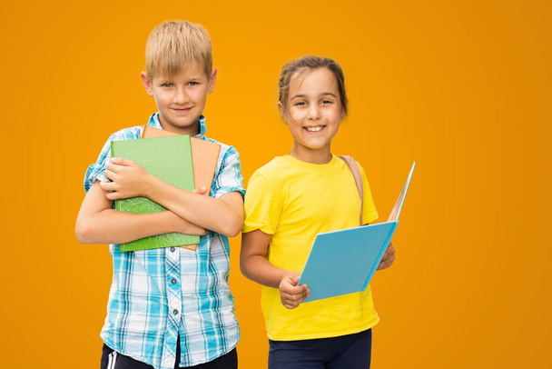 Photo of two small girl boy schoolchildren brother sister classmates hold books isolated orange color background. - Φωτογραφία, εικόνα