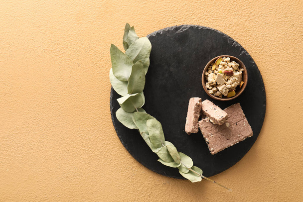 Board of tasty sesame halva with pistachios and eucalyptus branch on color background - Foto, immagini