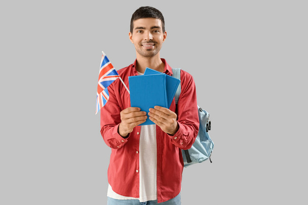 Young man with UK flag, books and backpack on grey background - Foto, imagen