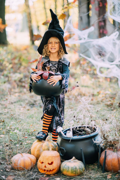 Beautiful girl witch. little girl in which costume celebrate Halloween outdoor and have fun. Kids trick or treating. girl witch with magic Book of spells. - Zdjęcie, obraz