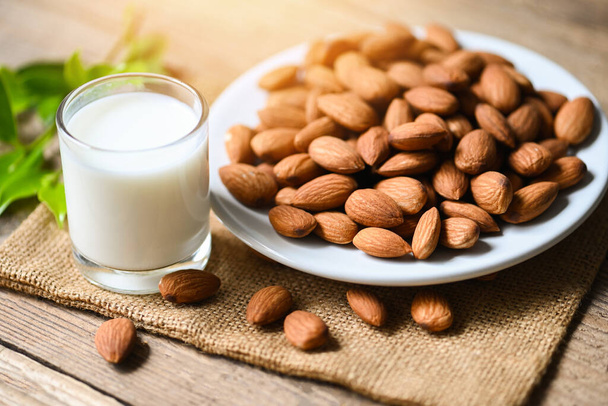 Almond milk and Almonds nuts on white plate background, Delicious sweet almonds on wooden table, roasted almond nut for healthy food and snack - Photo, image