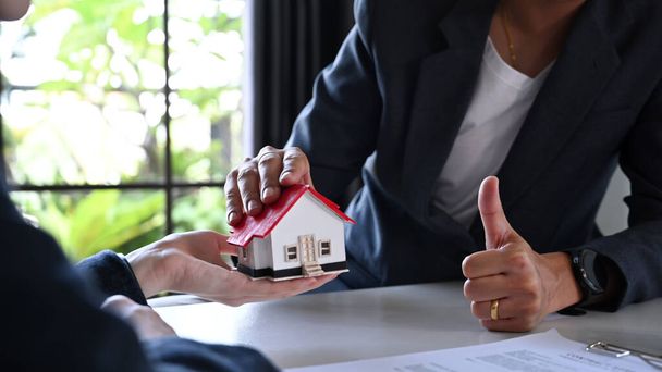 Cropped shot of businessman holding house model and showing thumb up sign approve excellent quality or mortgage offer. - Foto, afbeelding