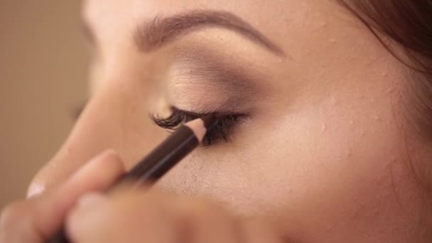 Make-up artist draws a line with a pencil over eyelashes, paints the eye, close-up. High quality footage - Video
