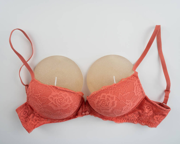 Breast implants in an orange bra on a white background - Zdjęcie, obraz