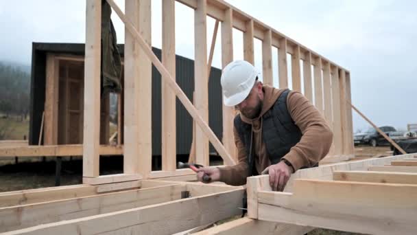 Man bouwend houten frame huis op paalfundering. Timmerman hameren spijker in houten plaat, met behulp van hamer. Timmermansconcept. - Video