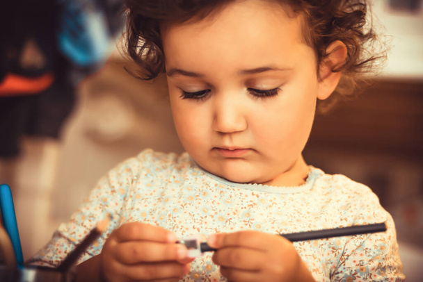 Little girl sharpening crayons while drawing at home.  - Foto, afbeelding