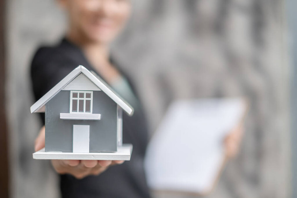 Koncepcja ubezpieczenia domu i nieruchomości. Bizneswoman trzyma model domu pracujący w inwestycjach o wynajmie domu, kupnie domu i ubezpieczenia domu. - Zdjęcie, obraz