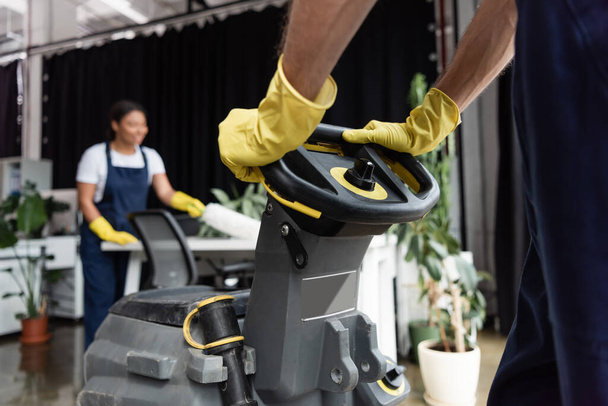 cropped view of man in rubber gloves operating floor scrubber machine near blurred bi-racial woman - Foto, imagen
