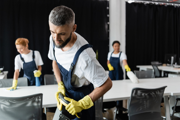 man with floor scrubber machine near interracial women cleaning desks on blurred background - Fotografie, Obrázek