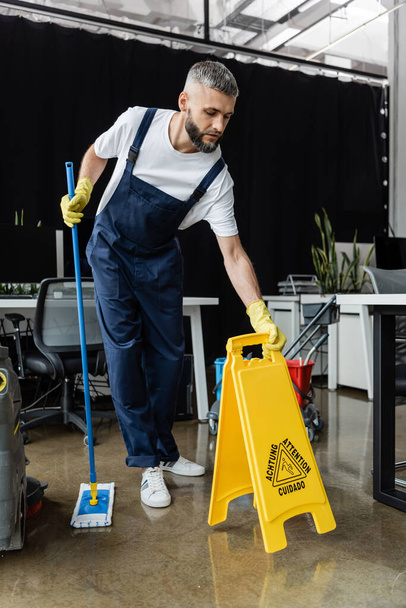 Limpiador profesional en overoles con fregona y cartelera de precaución en la oficina - Foto, Imagen