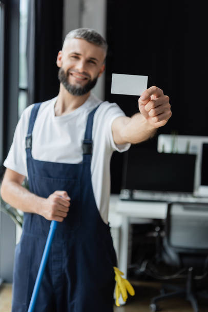 selective focus of empty business card in hand of smiling professional cleaner - Valokuva, kuva