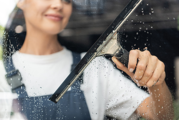 vista parcial del vidrio de lavado de mujer borrosa con escobilla de ventana - Foto, Imagen