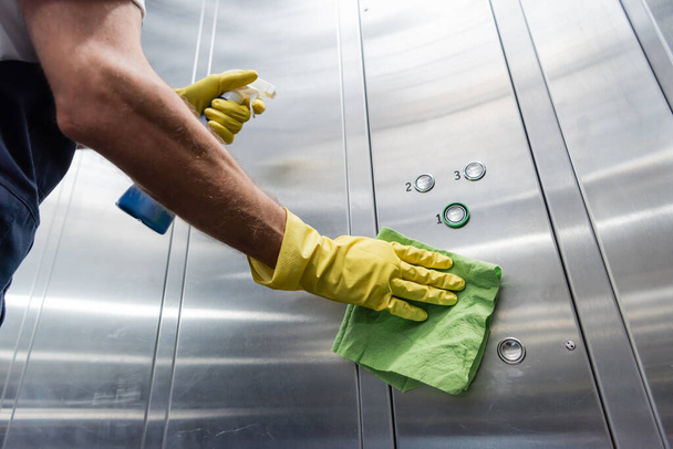 Ausgeschnittene Ansicht eines Mannes in Gummihandschuhen, der Fahrstuhl mit Waschmittel und Lappen reinigt - Foto, Bild
