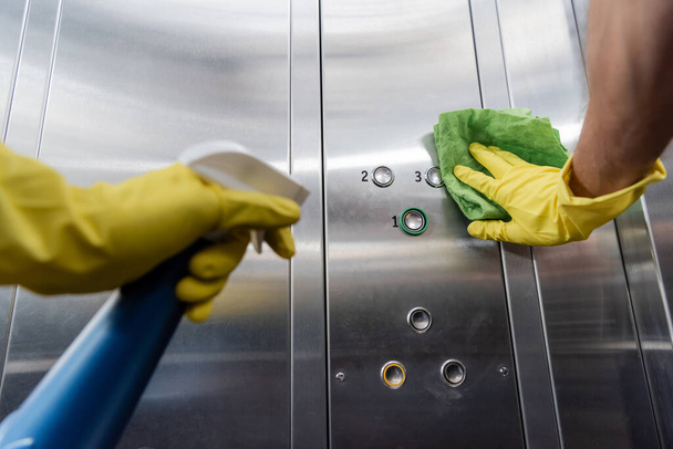 Vista parcial del limpiador en guantes de goma con detergente y botones de limpieza en ascensor - Foto, imagen