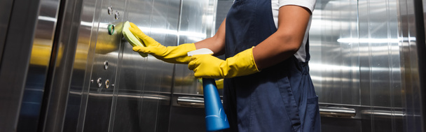 przycięty widok bi-rasowy czyściciel w odzieży roboczej i rękawic gumowych czyszczenie biurowe winda, baner - Zdjęcie, obraz