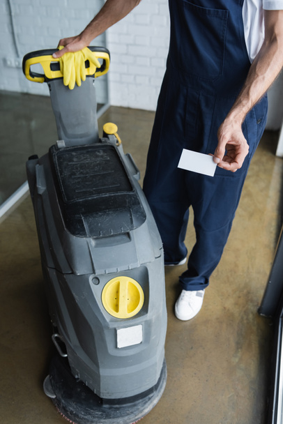 partial view of cleaner standing near floor scrubber machine and holding blank business card - Photo, Image