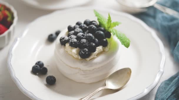 Delicious mini Pavlova μαρέγκα φωλιά με βατόμουρο και φύλλα δυόσμου σερβίρεται σε λευκό πιάτο - Πλάνα, βίντεο