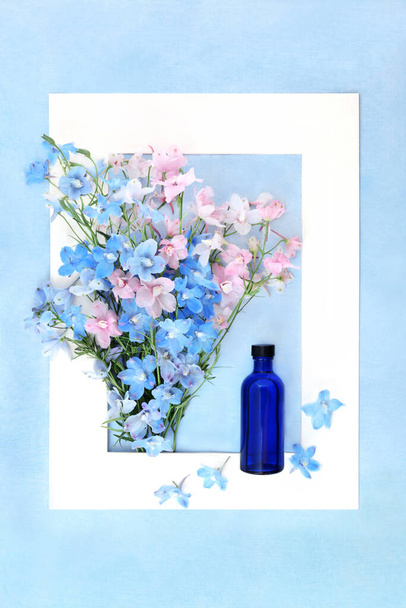 Delphinium Wildflower naturopathic medicina a base de hierbas con tintura botella de vidrio azul. Flora de verano composición de la naturaleza utilizada en la medicina herbal como sedante. Marco blanco sobre azul moteado. - Foto, Imagen