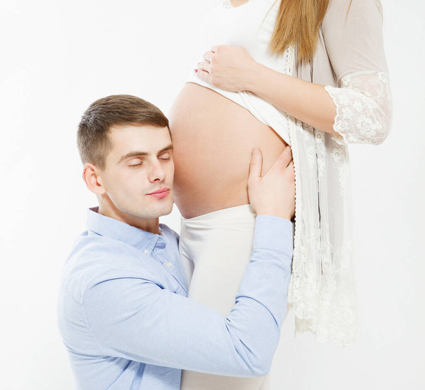 Beau homme écoute le ventre de sa belle femme enceinte avec les yeux fermés - Photo, image