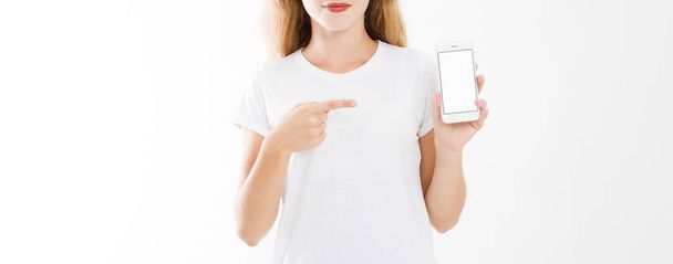young girl, woman in t-shirt pointing finger at blank screen mobile phone isolated on white background. Hand holding smartphone. Copy space - Фото, изображение