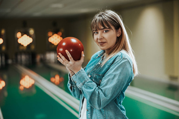 Shot of a cute young woman holding bowling ball at the bowling club and looking at camera. - Fotografie, Obrázek