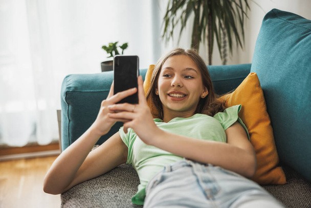 Beautiful teenager girl surfing social media on smart phone while having leisure time at her home. - Fotoğraf, Görsel