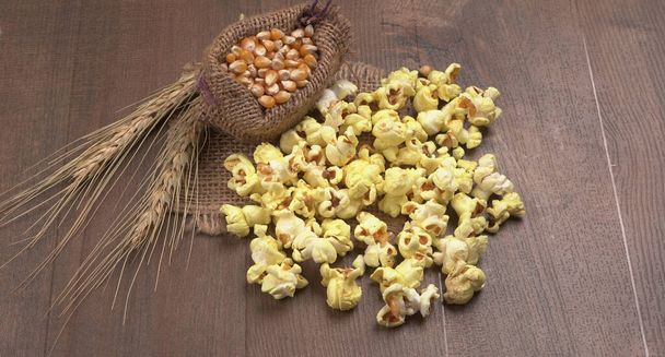 Kupa pysznego popcornu z surowymi ziarnami kukurydzy w worku na drewnianym stole. - Zdjęcie, obraz