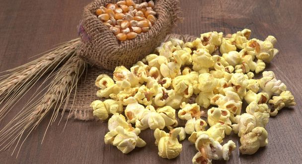 Heap herkullisia popcornia raaka maissi siemenet säkissä puinen pöytä. - Valokuva, kuva