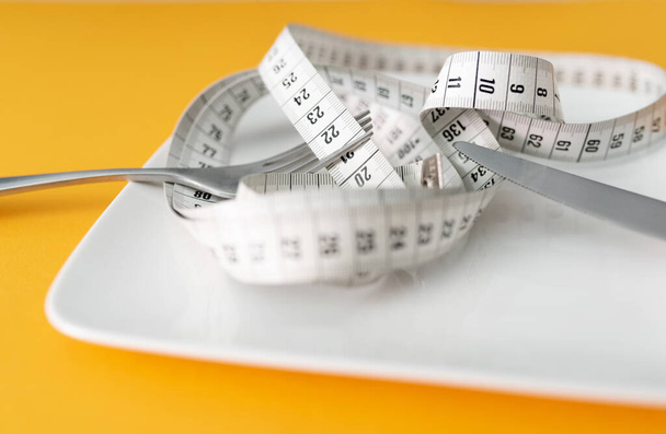 tape measure on plate with fork and knife against orange table background, dieting and loosing weight concept - Fotografie, Obrázek