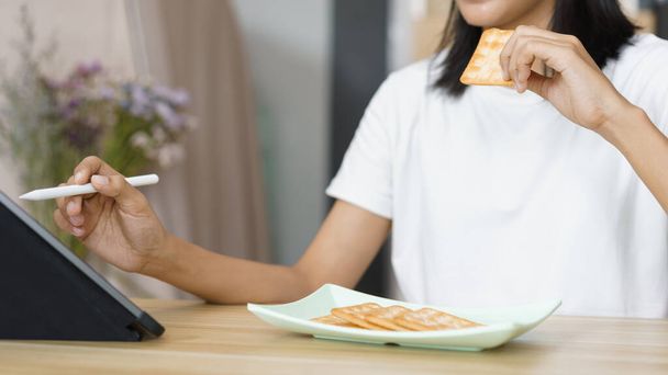 Concept de style de vie à la maison, Jeune femme utilisant une tablette et manger des craquelins pendant ses loisirs à la maison. - Photo, image