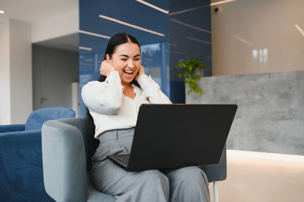 Portrait of excited young caucasian woman celebrating success while sitting with laptop at home or modern office Happy female freelancer working in coworking space. - Foto, afbeelding