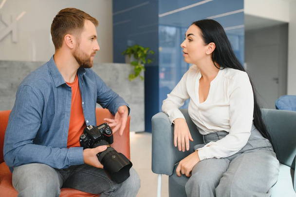 Young photographer man in blue shirt watching photo with client woman after photo session and smiling and looking at each other. - Valokuva, kuva