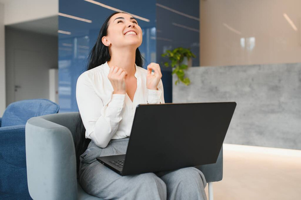 Portrait of excited young caucasian woman celebrating success while sitting with laptop at home or modern office Happy female freelancer working in coworking space. - Zdjęcie, obraz