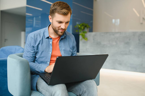 happy smiling remote online working man in casual outfit with laptop in joyful successful winning gesture sitting in an coworking office at a work desk - Photo, image