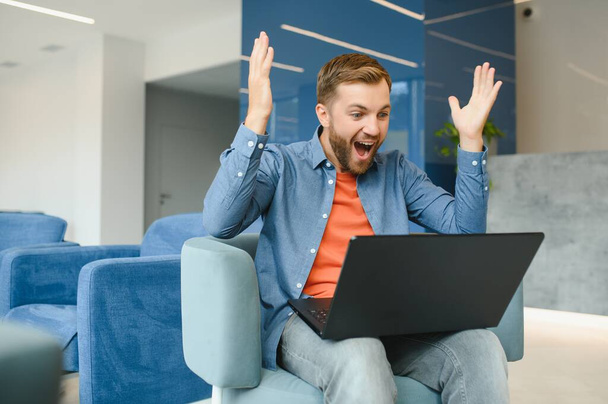 Photo of young excited man happy positive smile celebrate win victory success fists hands sit sofa home remote work - Foto, Imagem