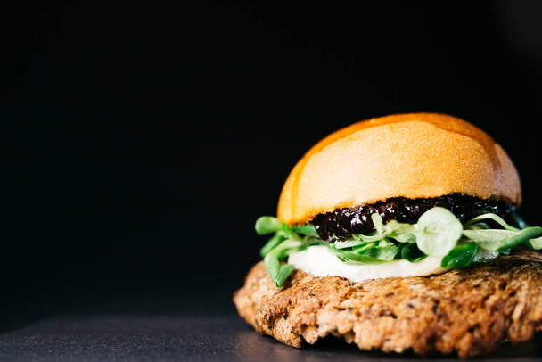 Doble burger with blueberries, vegetables and cheese over a black background - Photo, Image