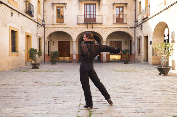 Flamenco-Mann mittleren Alters mit langen Haaren tanzt Flamenco auf einem Platz mit Säulen und Balkonen in Sevilla, Spanien. Spüren Sie die Leidenschaft. Flamenco-Tanzkonzept kulturelles Erbe der Menschheit. - Foto, Bild
