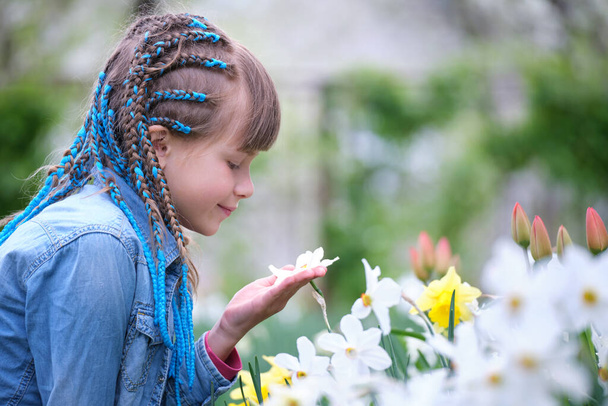 Glückliches Mädchen spielt im Sommergarten und genießt den süßen Duft weißer Narzissenblüten an sonnigen Tagen. - Foto, Bild