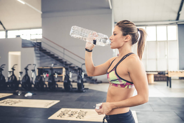 Young sportive woman indoors gym drinking water taking a break from training - Fotoğraf, Görsel