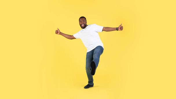 Cheerful African American Guy Gesturing Thumbs Up With Both Hands Approving Offer Posing Over Yellow Studio Background, Smiling To Camera. I Like It. Panorama - 写真・画像
