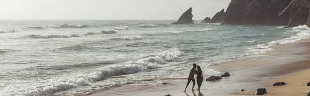 бородатый мужчина обнимает девушку в платье во время прогулки по океанской воде, баннер - Фото, изображение