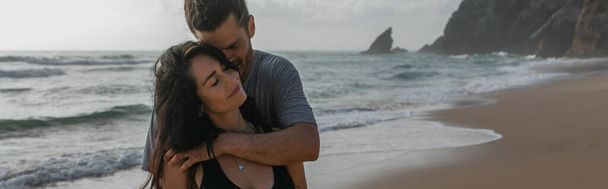 feliz hombre abrazando sonriente novia cerca del océano en portugal, bandera - Foto, imagen