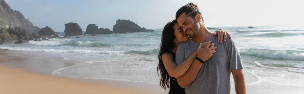 sonriente mujer abrazando feliz novio cerca de océano en portugal, bandera - Foto, Imagen