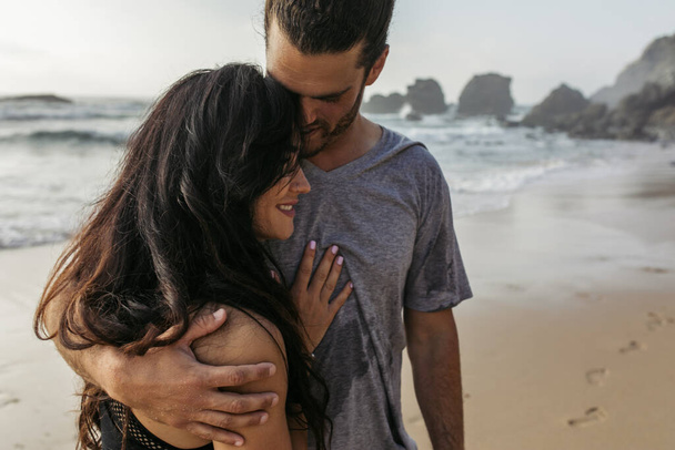 bearded man in grey t-shirt hugging happy girlfriend near ocean in portugal - Zdjęcie, obraz