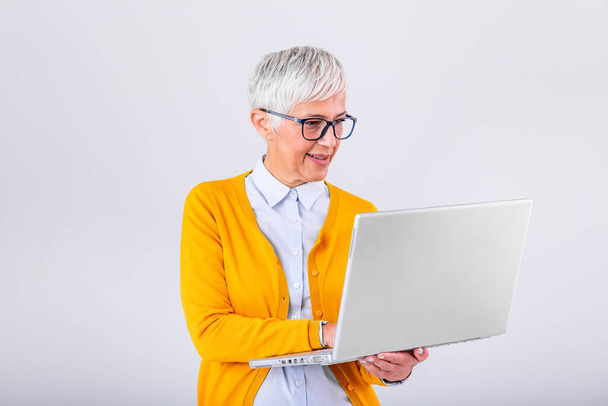 Зображення веселої зрілої жінки, що стоїть ізольовано на сірому фоні за допомогою ноутбука. Портрет усміхненої старшої леді, що тримає ноутбук
 - Фото, зображення