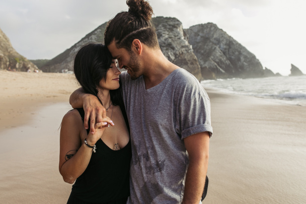 cheerful bearded man and tattooed woman in dress holding hands near ocean  - Zdjęcie, obraz