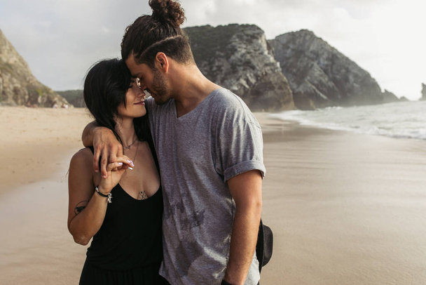 homme barbu joyeux et femme tatouée en robe tenant la main près de l'océan  - Photo, image