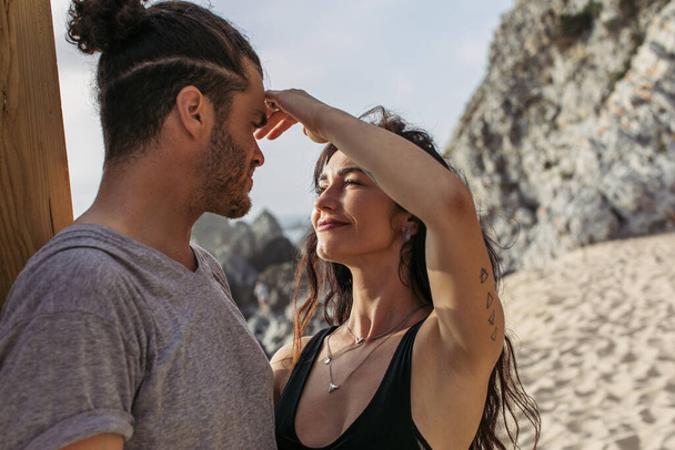 入れ墨女性タッチ顔のひげを生やしたボーイフレンドのビーチでポルトガル語 - 写真・画像