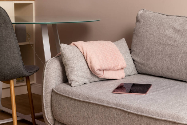 Cozy gray textile sofa with folded pink plaid and digital tablet - Foto, Imagem